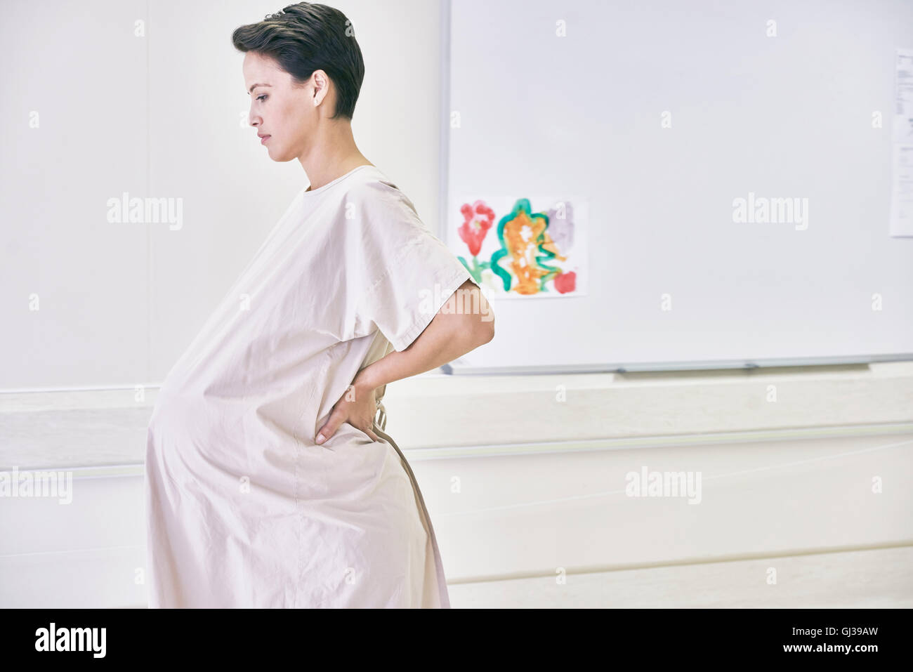 Vista laterale della donna incinta indossando abito ospedale Foto Stock