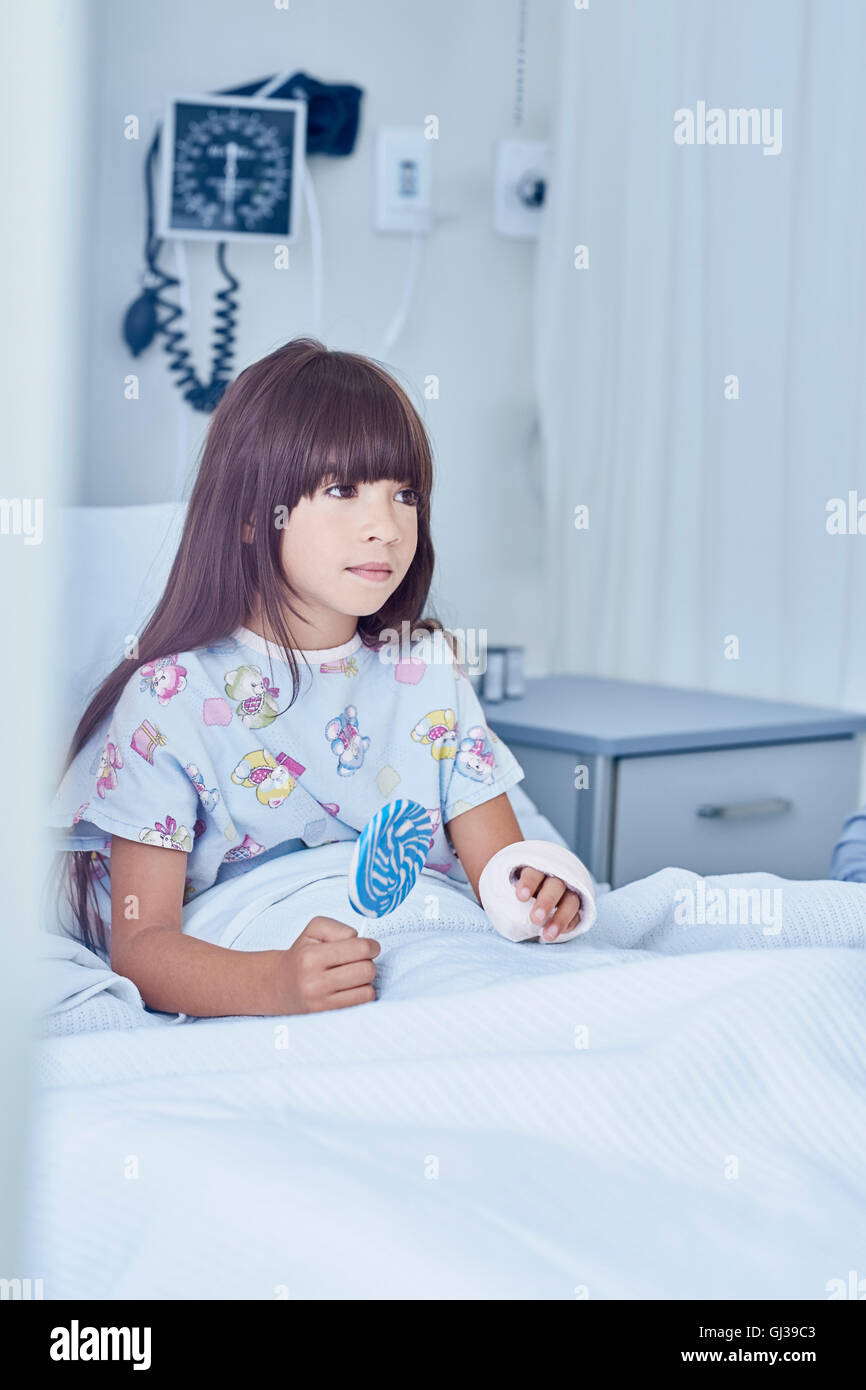 Ragazza paziente con braccio calco in gesso in letto con lollipop in ospedale per bambini ward Foto Stock