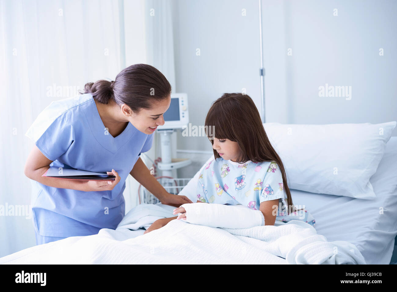 Infermiera femmina spiegare al paziente la ragazza con il braccio calco in gesso in ospedale per bambini ward Foto Stock