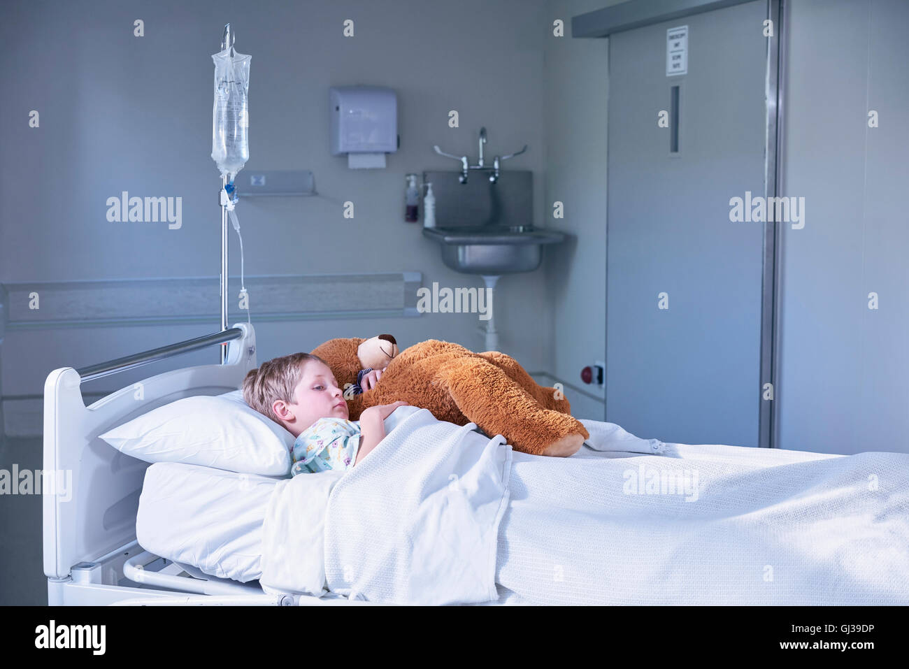 Ragazzo paziente nel letto abbracciando Teddy bear in ospedale per bambini ward Foto Stock