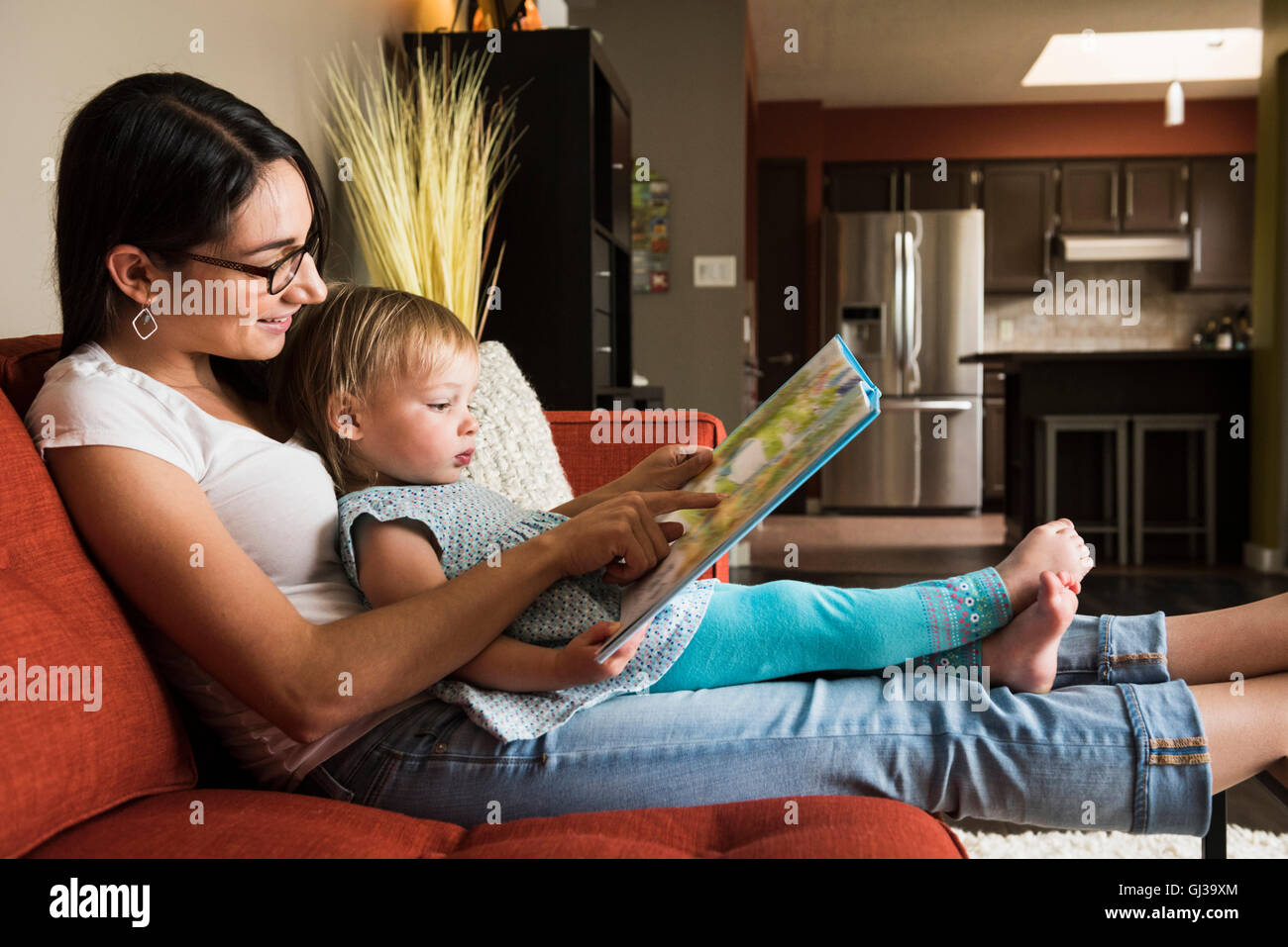 Madre figlia di insegnamento per leggere un libro sul divano Foto Stock