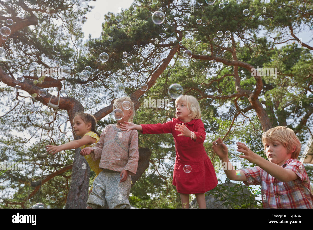 Piccolo gruppo di giovani amici a giocare all'aperto, guardando le bolle in aria Foto Stock
