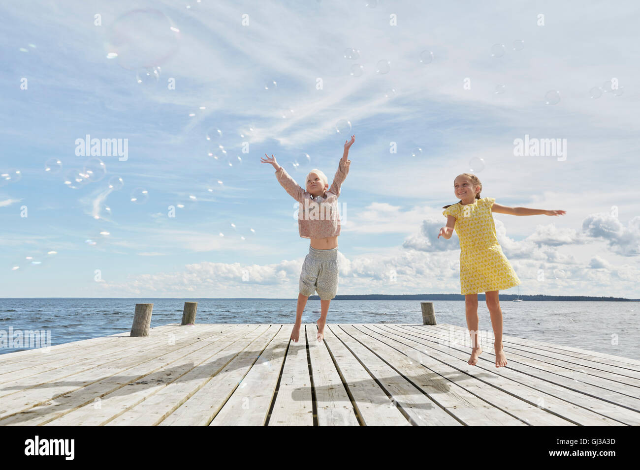 Due giovani amici sul molo in legno, saltando per raggiungere le bolle Foto Stock