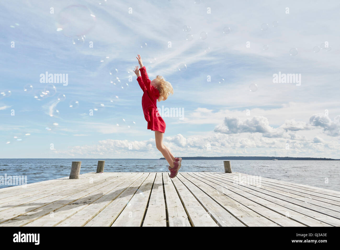 Giovane ragazza sul molo in legno, saltando per raggiungere le bolle Foto Stock