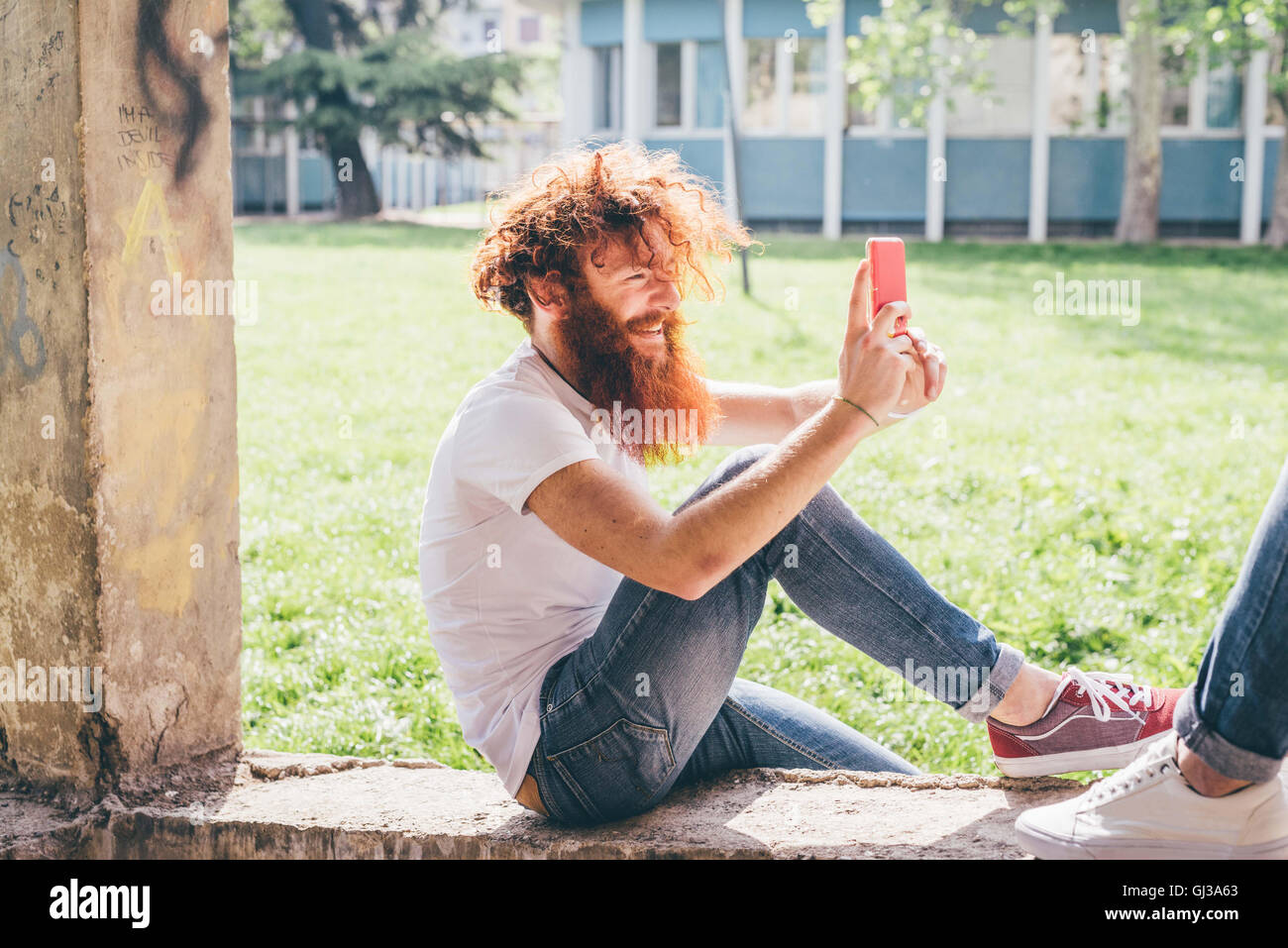 Giovane maschio hipster con rosso di capelli e la barba di fotografare amico sullo smartphone in posizione di parcheggio Foto Stock