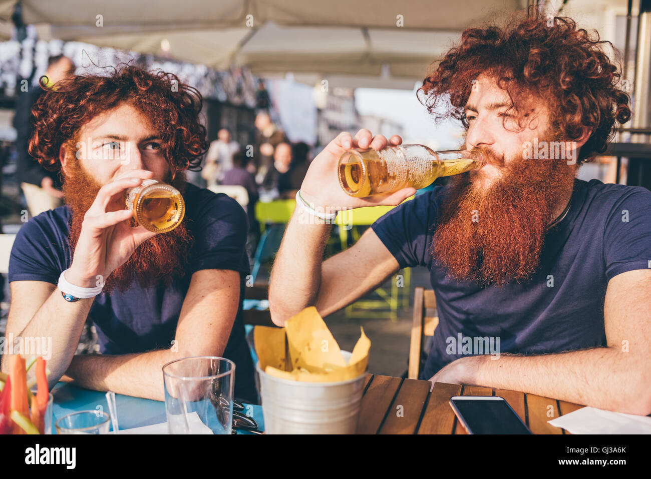 Giovane maschio hipster gemelli con i capelli rossi e le barbe di bere birra al bar sul marciapiede Foto Stock