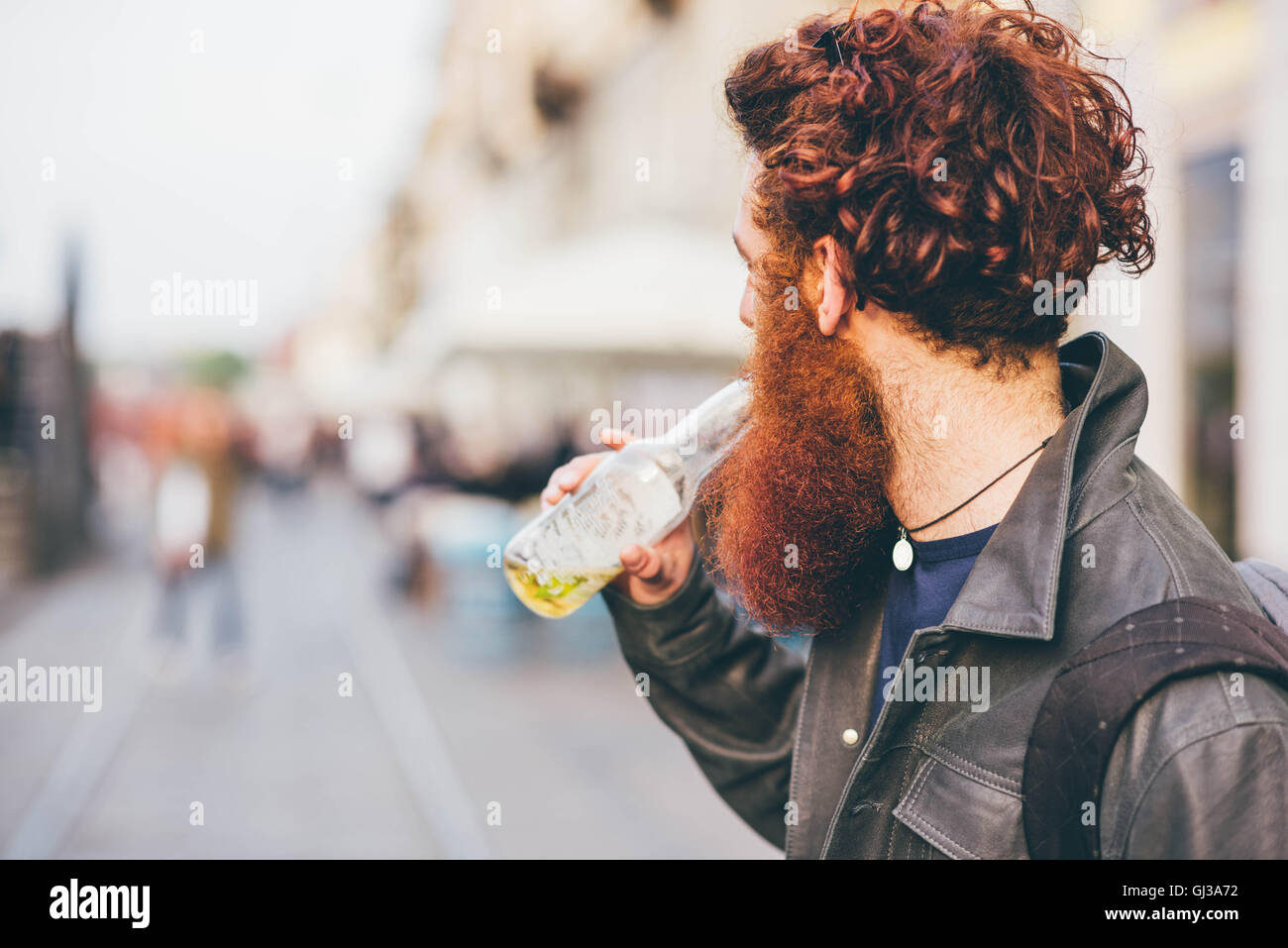 Giovane maschio hipster con rosso di capelli e la barba di bere la birra in bottiglia sulla strada di città Foto Stock