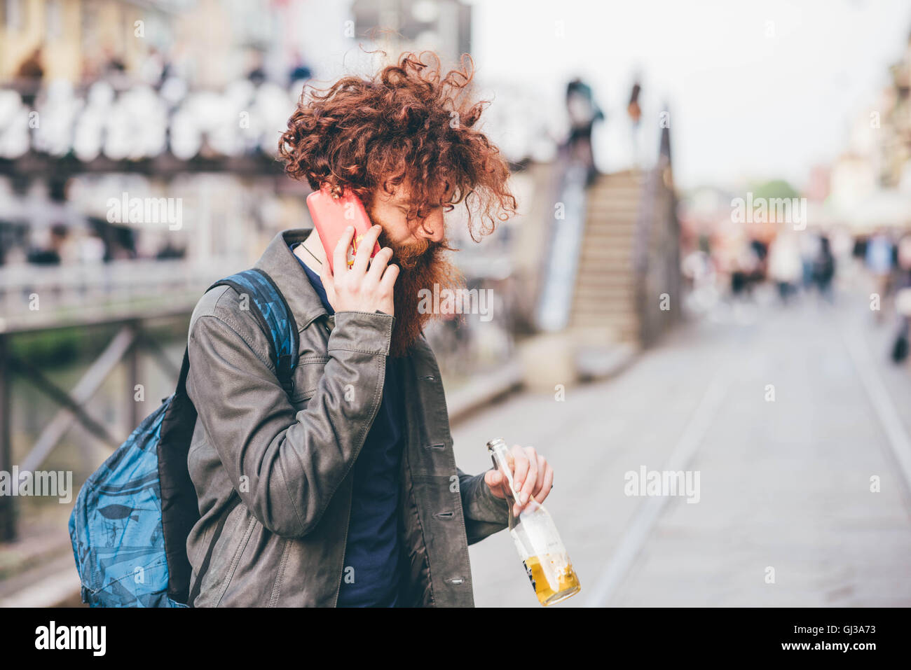 Giovane maschio hipster con i capelli rossi e la barba a chattare su smartphone su una strada di città Foto Stock