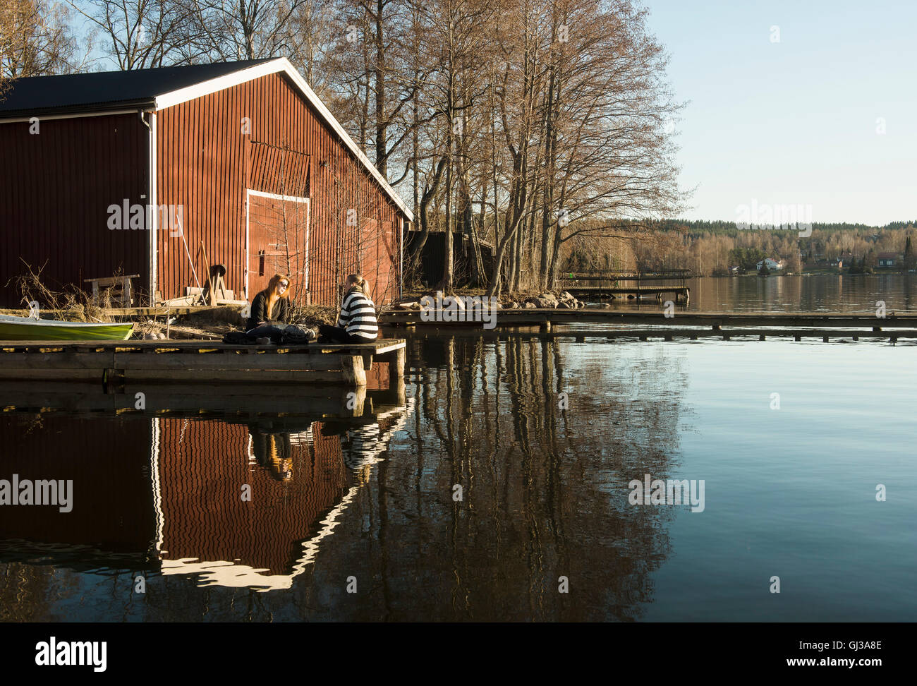 Due donne sedute in chat sul molo presso il lago Vesijarvi, Lahti, Finlandia Foto Stock