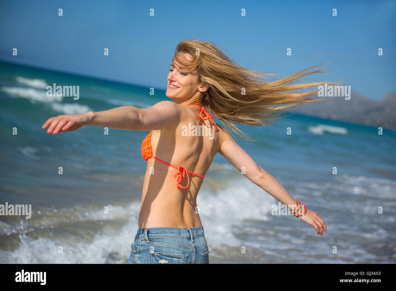 Giovane donna sulla spiaggia, braccia tese, sorridente Foto Stock