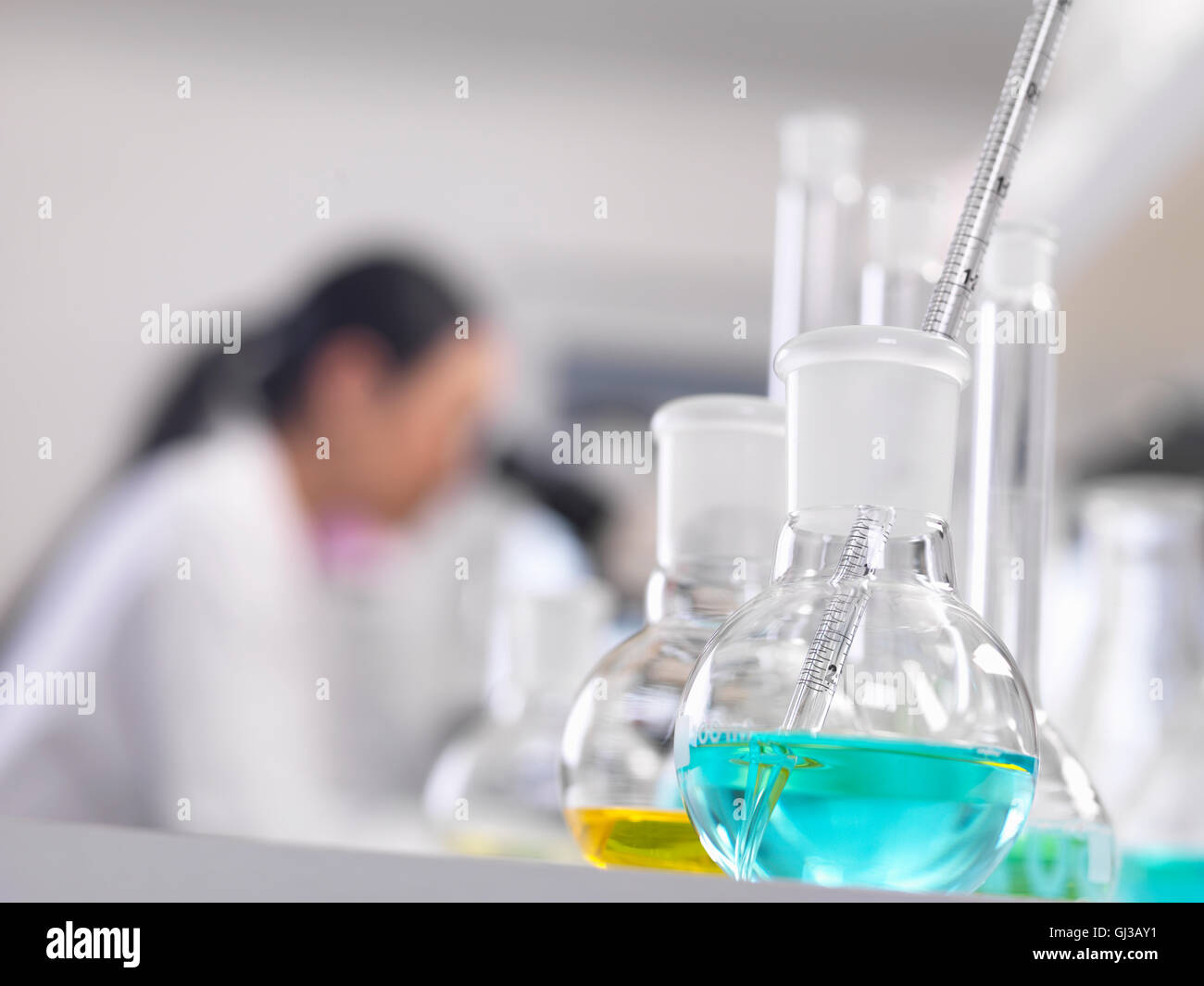 Uno scienziato guardando giù un microscopio con una formula chimica in primo piano Foto Stock