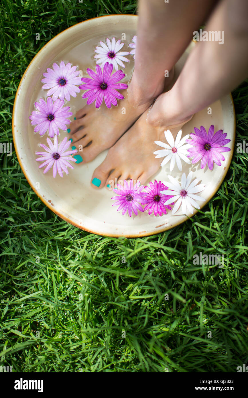 Giovane donna i piedi in un recipiente di acqua di fiori sul prato Foto Stock