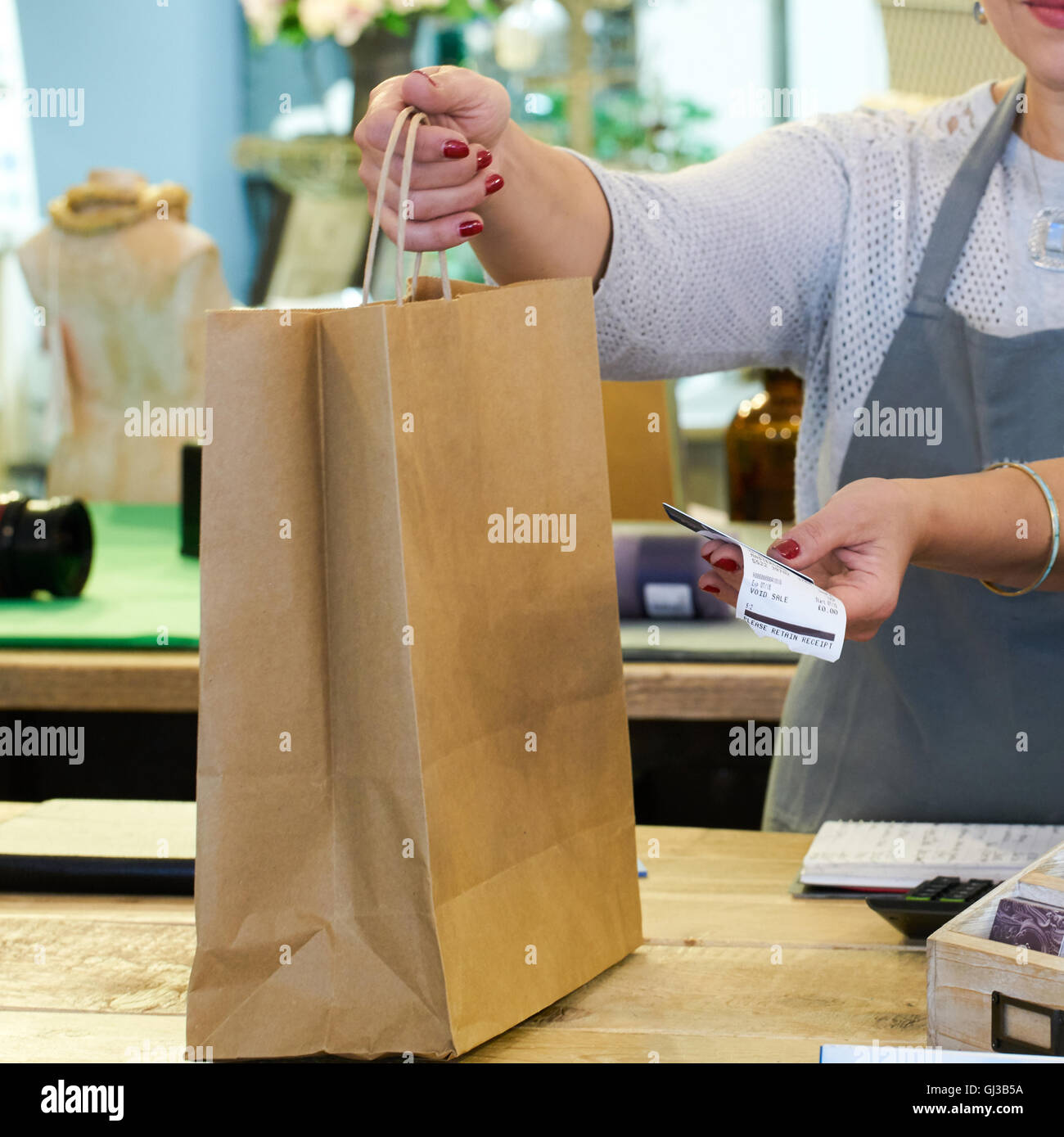 Ritagliato colpo di assistente di vendita consegna shopping bag e ricevuta in dono checkout negozio Foto Stock