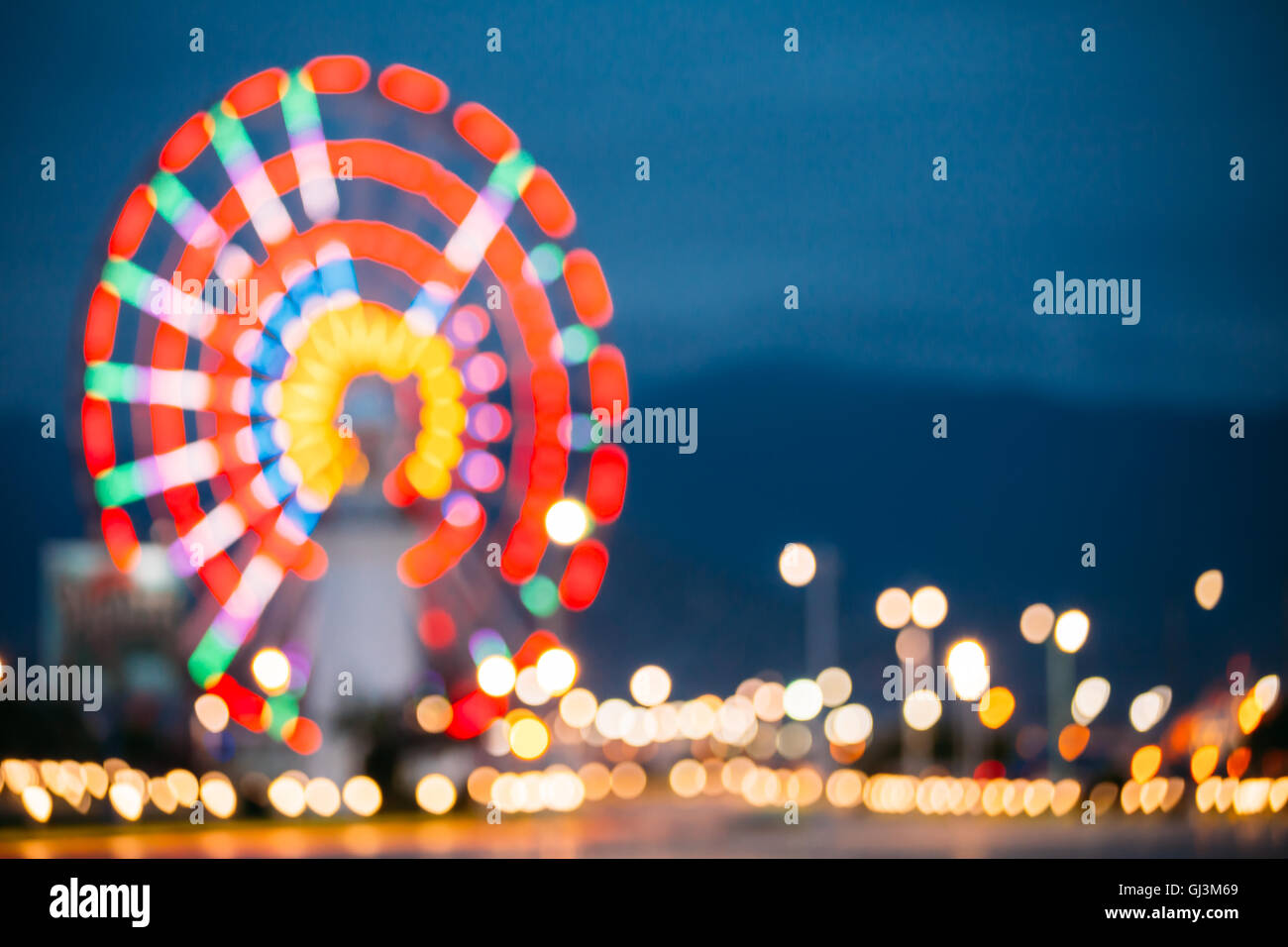Abstract sfocatura di immagine colorata luminosamente illuminata ruota panoramica Ferris nella città di divertimenti Parco su nero blu del cielo della sera Bokeh di fondo Foto Stock