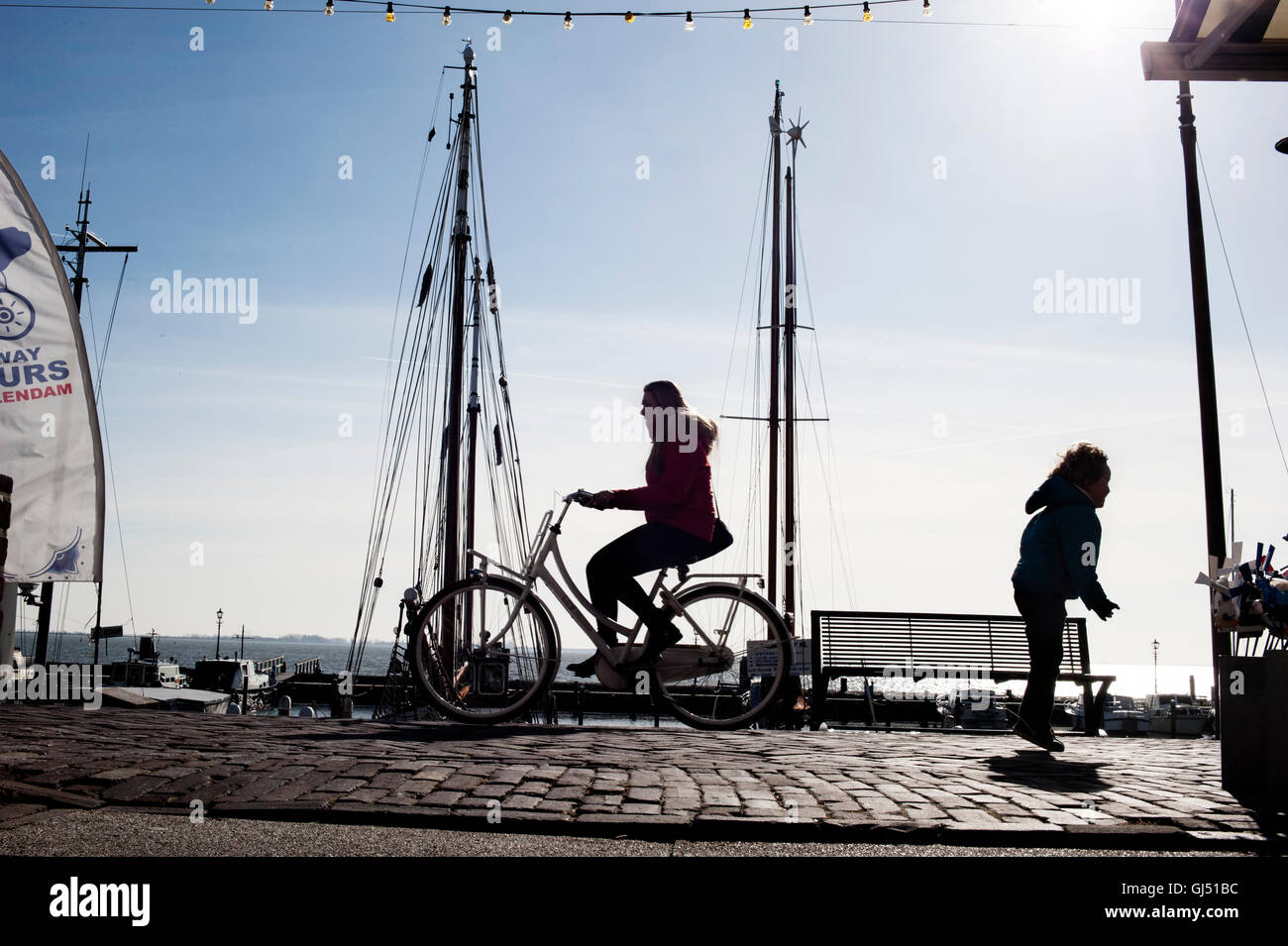Una silhouette di un bambino del salto e un ciclista sul fronte mare a Volendam, Paesi Bassi Foto Stock