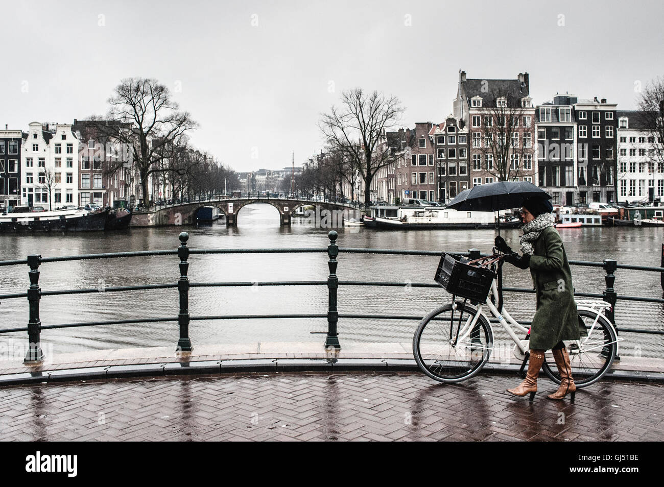 Una donna con una bicicletta sotto la pioggia su un ponte in Amsterdam Foto Stock