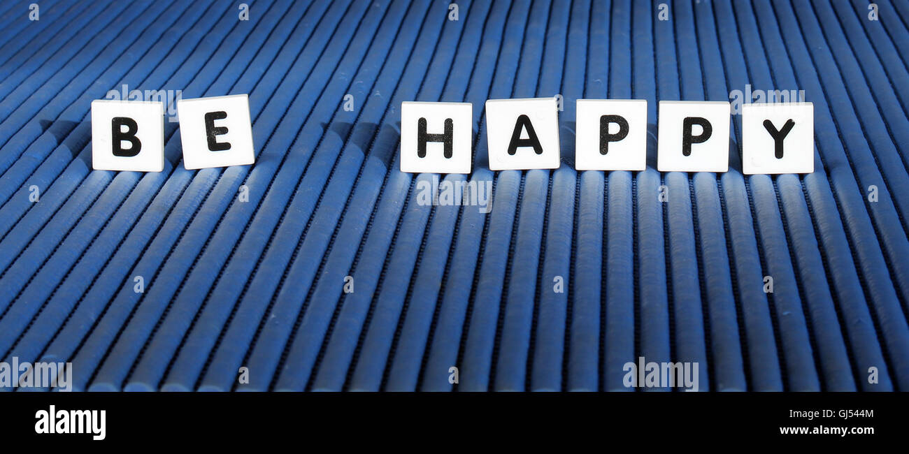 "Essere felice' lettera piastrelle ancora vita su sfondo blu Foto Stock