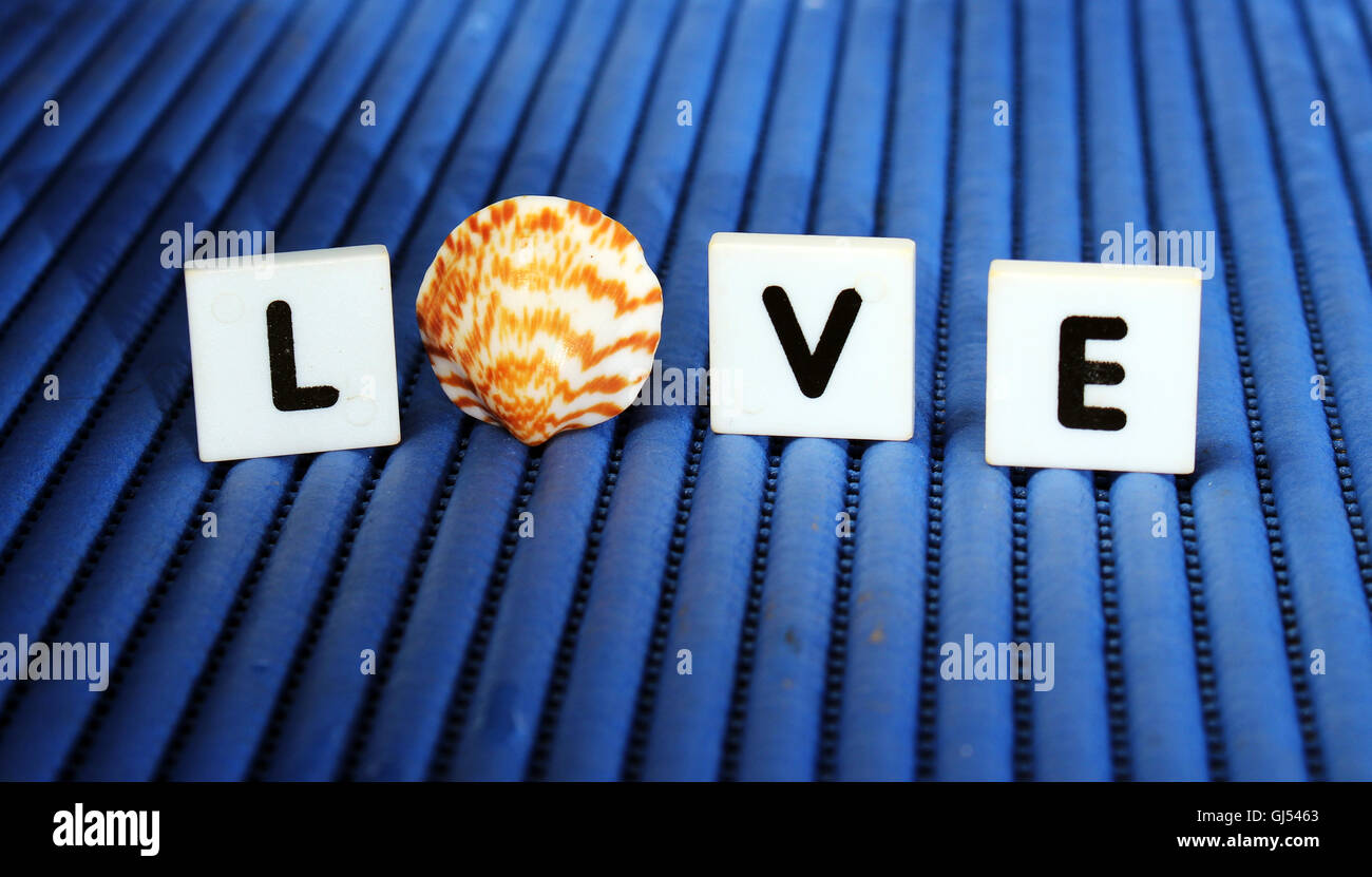 "L'amore" lettera piastrelle e conchiglia di mare ancora in vita con sfondo blu Foto Stock