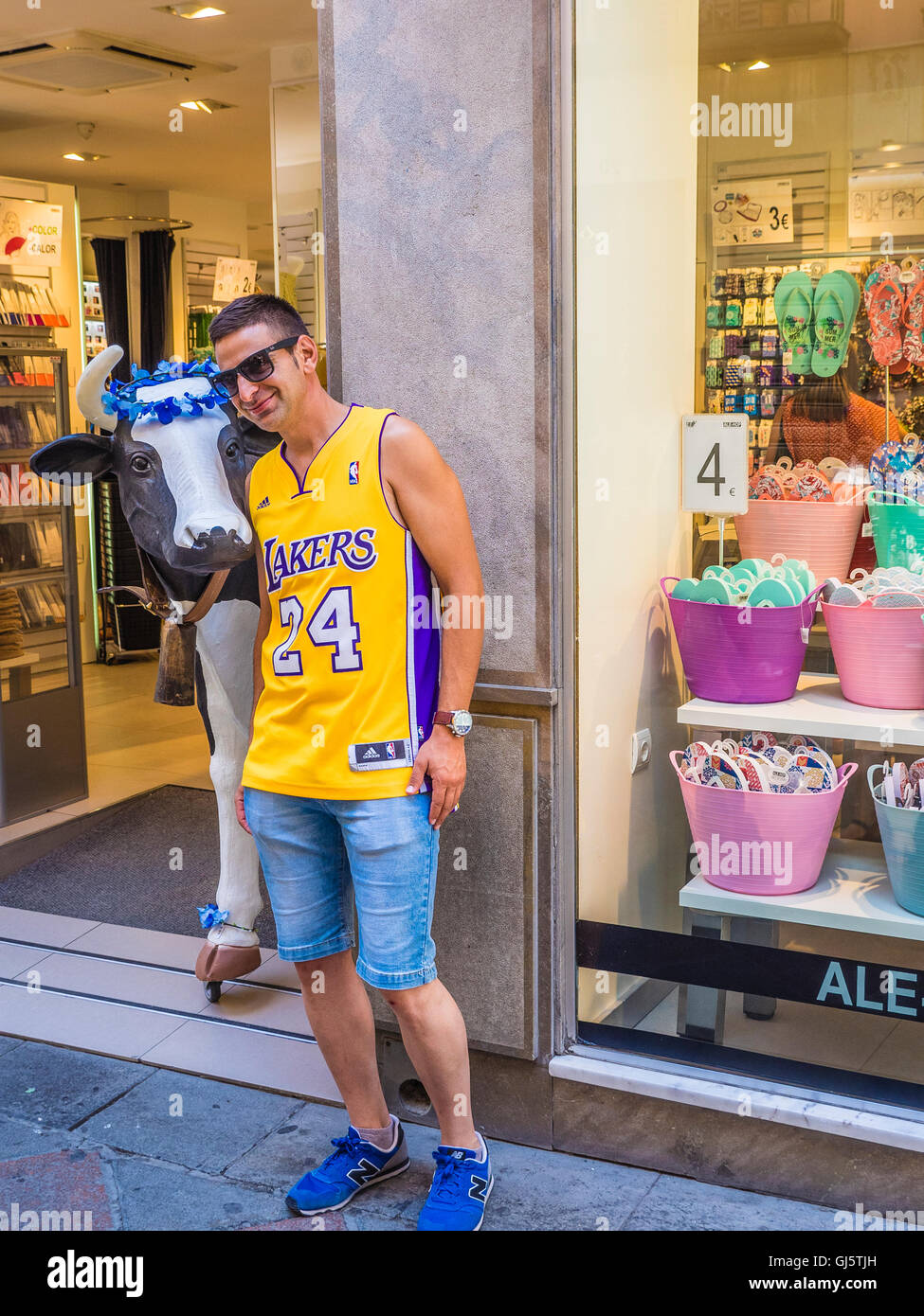 Un turista maschio indossando un Los Angeles Lakers basketball jersey team pone con una vita artificiale di vacca dimensioni al di fuori di un negozio. Foto Stock