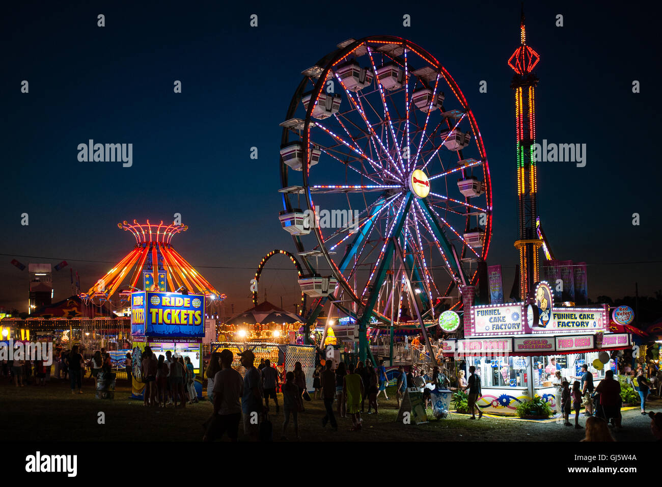 Ruota panoramica illuminata dai colori vivaci e giostre di carnevale sono colorate attrazioni notturne alla fine della fiera estiva della contea di Cecil Co., Maryland, USA. Foto Stock