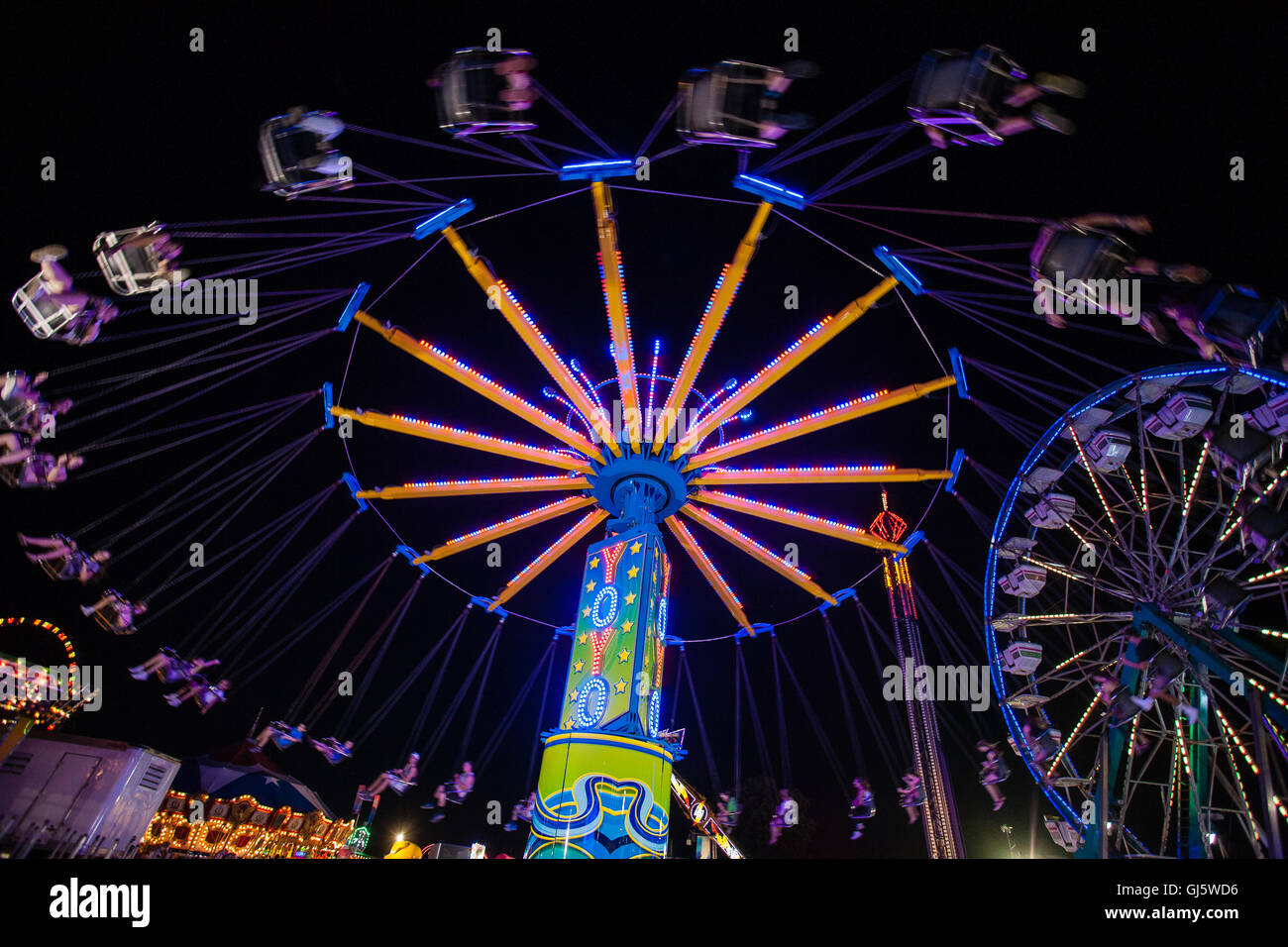 Ruota panoramica illuminata dai colori vivaci e giostre di carnevale sono colorate attrazioni notturne alla fine della fiera estiva della contea di Cecil Co., Maryland, USA. Foto Stock