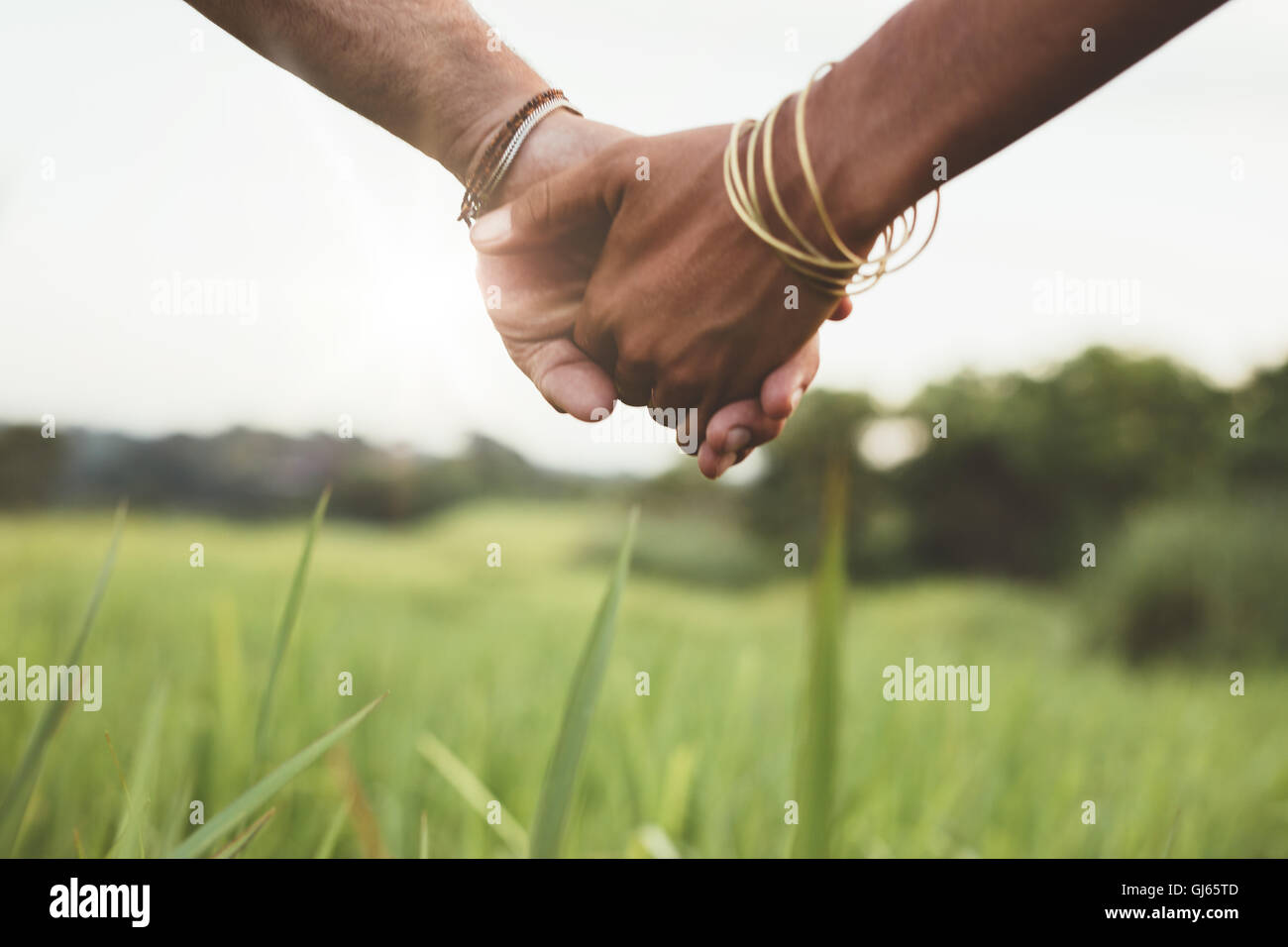 Immagine ravvicinata di coppia giovane tenendo le mani nel campo all'esterno. Uomo e donna mano nella mano sul prato. Foto Stock
