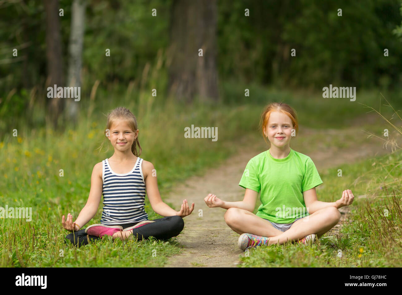 Due piccoli cute ragazze seduta nella posizione del loto nel parco. Lo yoga e uno stile di vita sano. Foto Stock