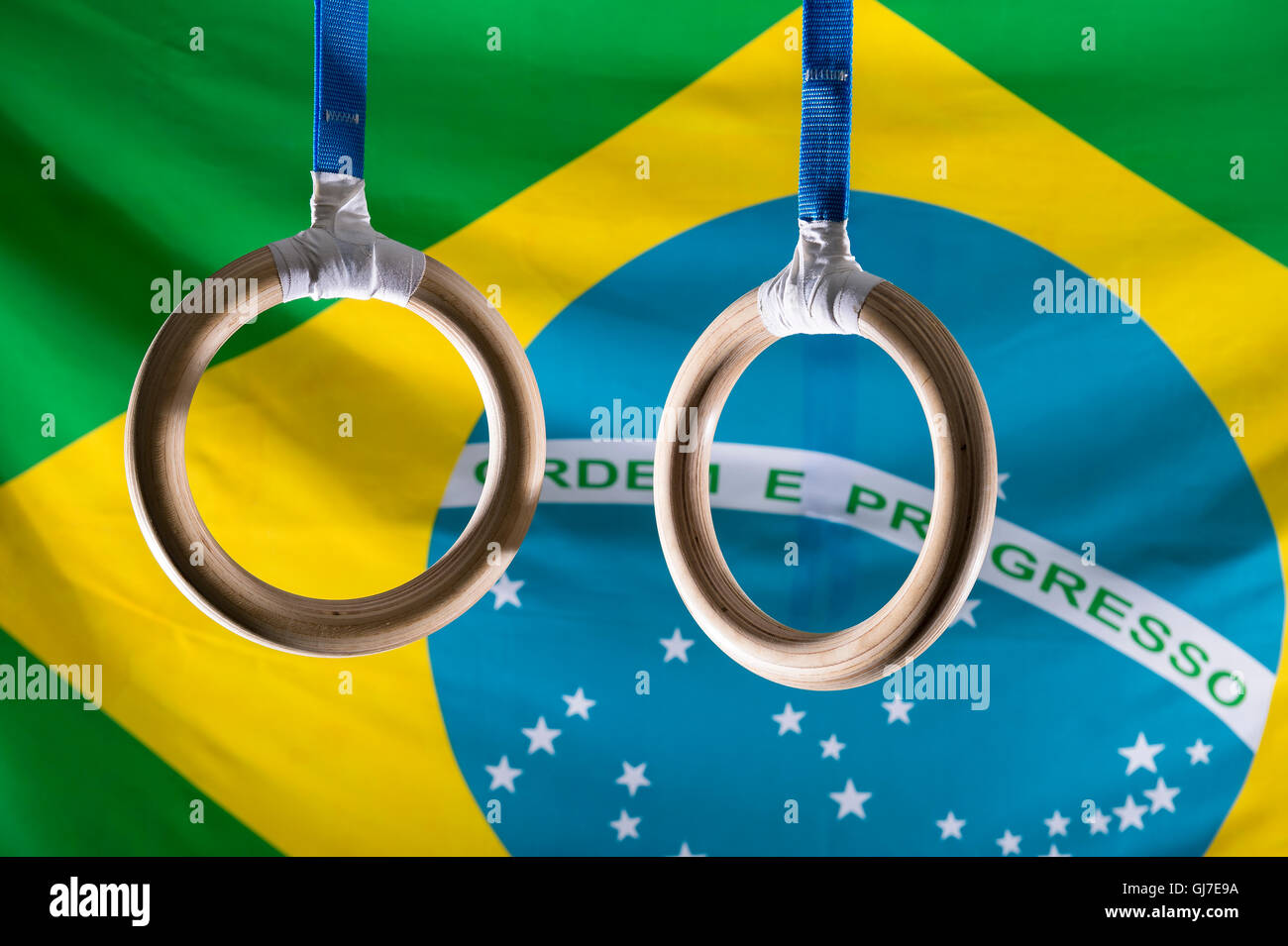 Anelli ginnasta pendenti davanti drammaticamente illuminati bandiera brasiliana sfondo Foto Stock