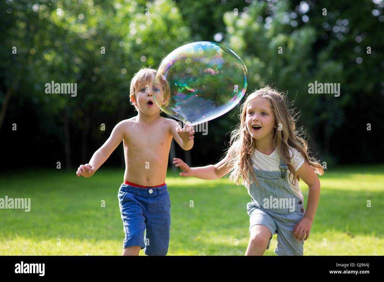 Proprietà rilasciato. Modello rilasciato. Fratello e Sorella a caccia di bolle nel giardino. Foto Stock