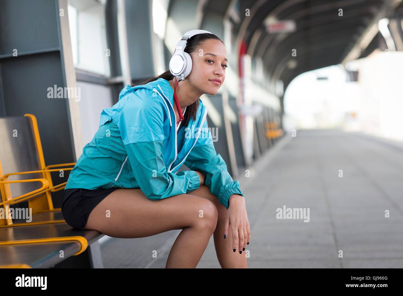 Modello rilasciato. Giovane donna seduta sulla piattaforma ferroviaria di indossare le cuffie. Foto Stock