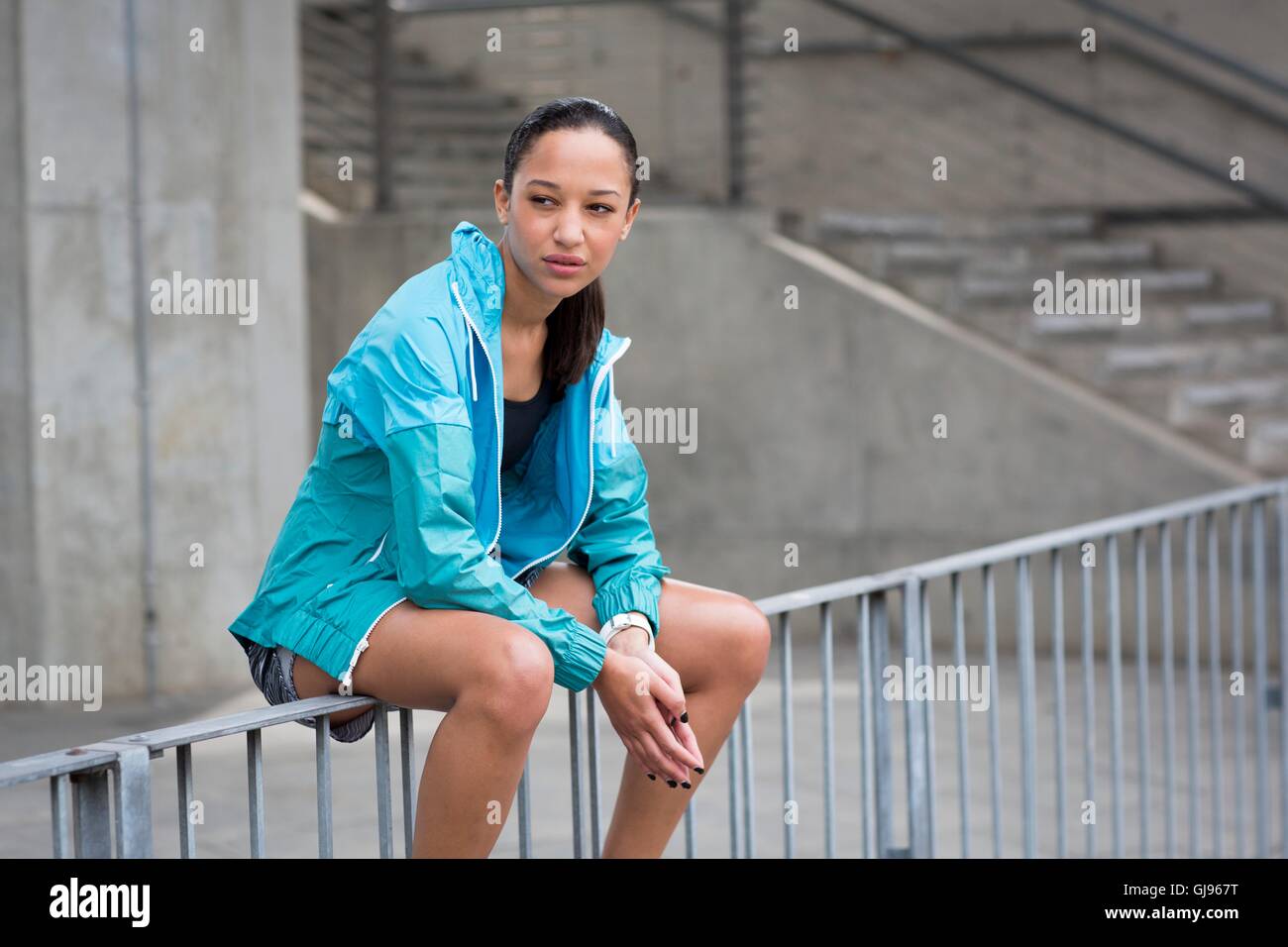 Modello rilasciato. Ritratto di giovane donna seduta sulle ringhiere che guarda lontano. Foto Stock