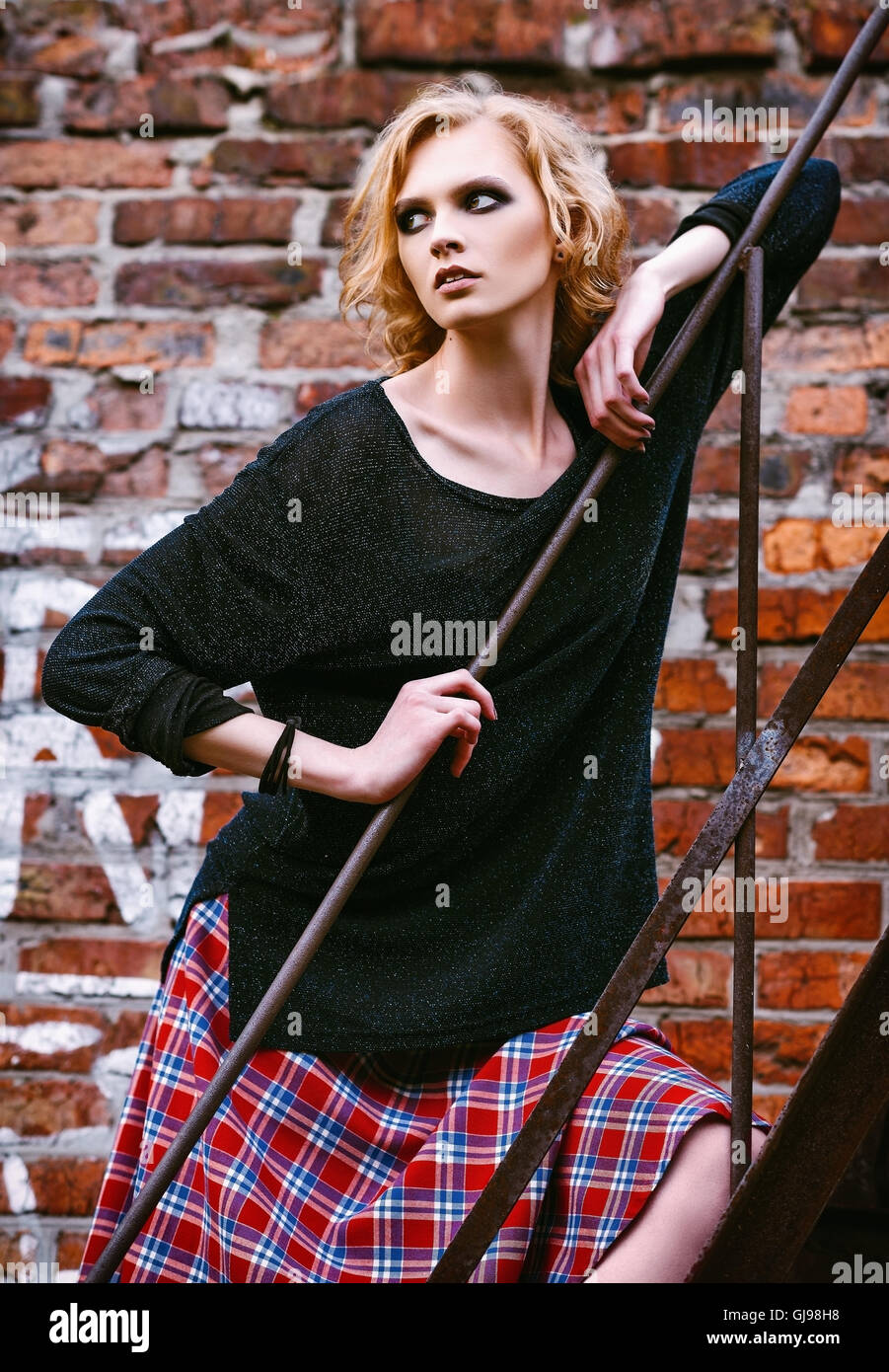 Grunge fashion: cute giovane donna in a scacchi in gonna e giacca in piedi sulla scaletta Foto Stock