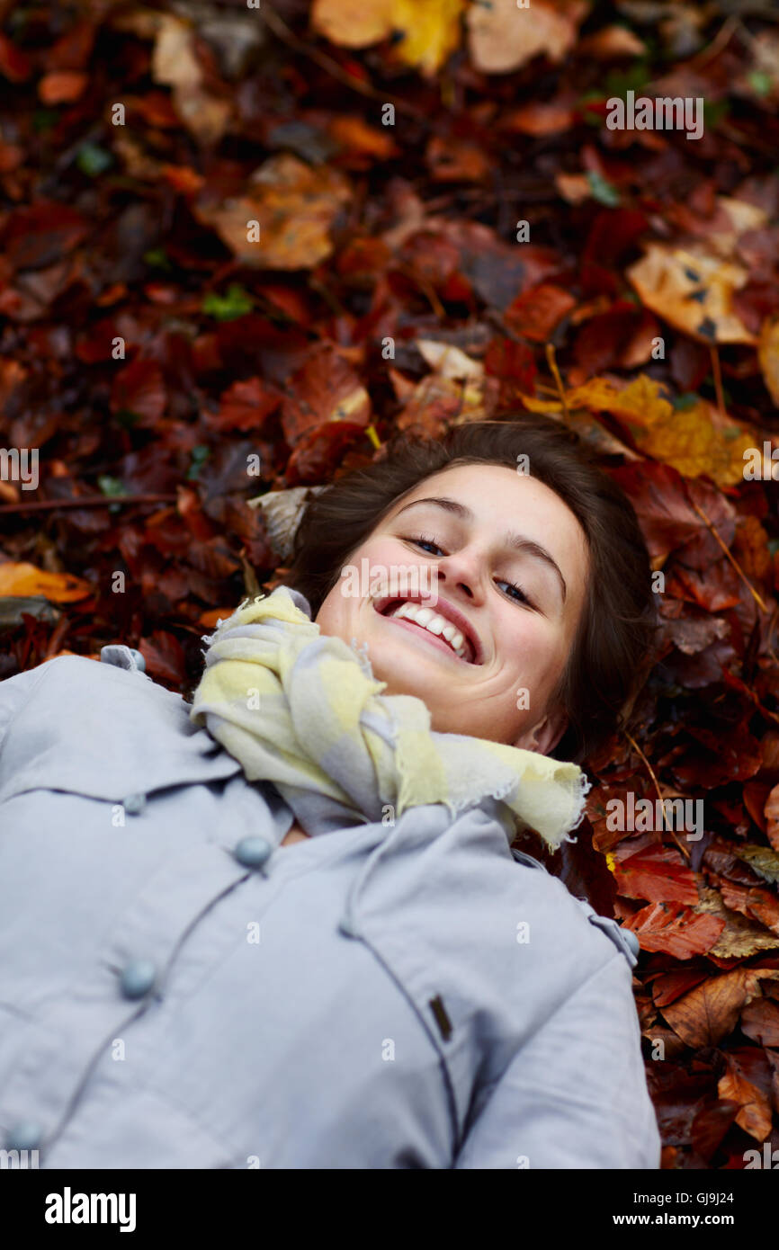 Sorridente ragazza adolescente giacente in foglie di autunno Foto Stock