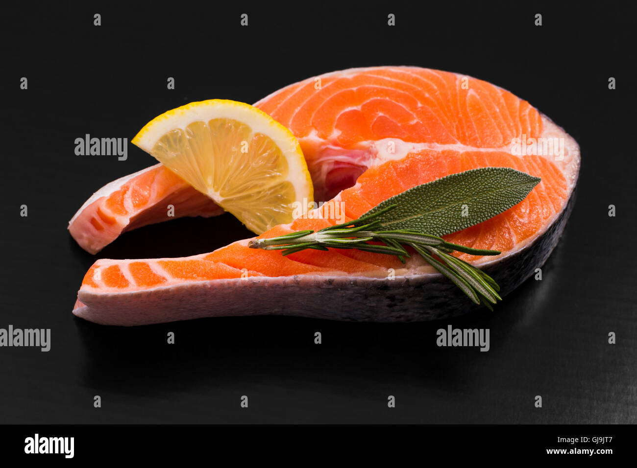 Fetta di bistecca di salmone con limone e erbe su nero Foto Stock