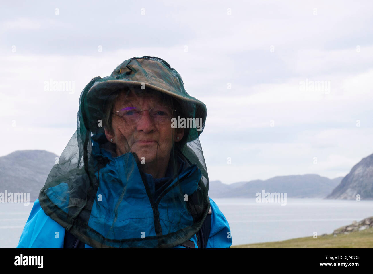 Un anziano turista femminile che indossa una zanzariera per proteggere dalle punture di insetti in una regione rurale sulla costa. Qaqortoq Groenlandia Foto Stock