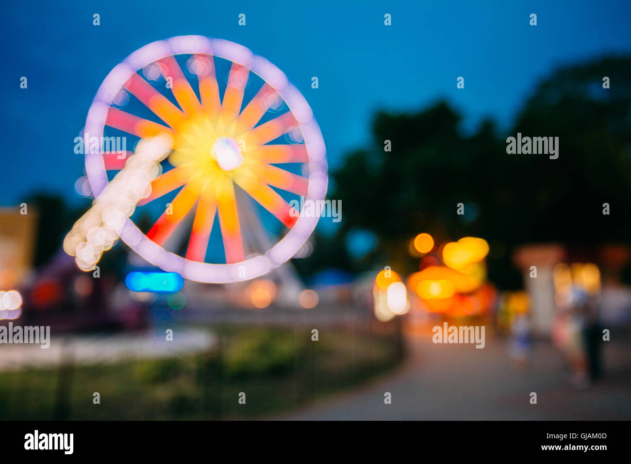 Abstract sfocatura di immagine colorata luminosamente illuminata ruota panoramica Ferris nella città di divertimenti Parco su nero blu del cielo della sera Bokeh di fondo Foto Stock