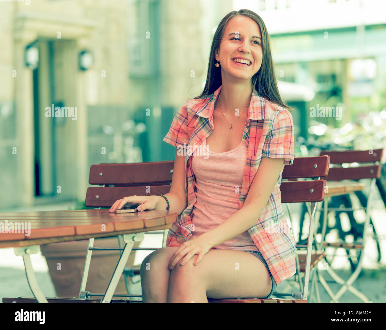 Giovane donna che indossano pantaloncini sede a tavola in street cafe e sorridente Foto Stock