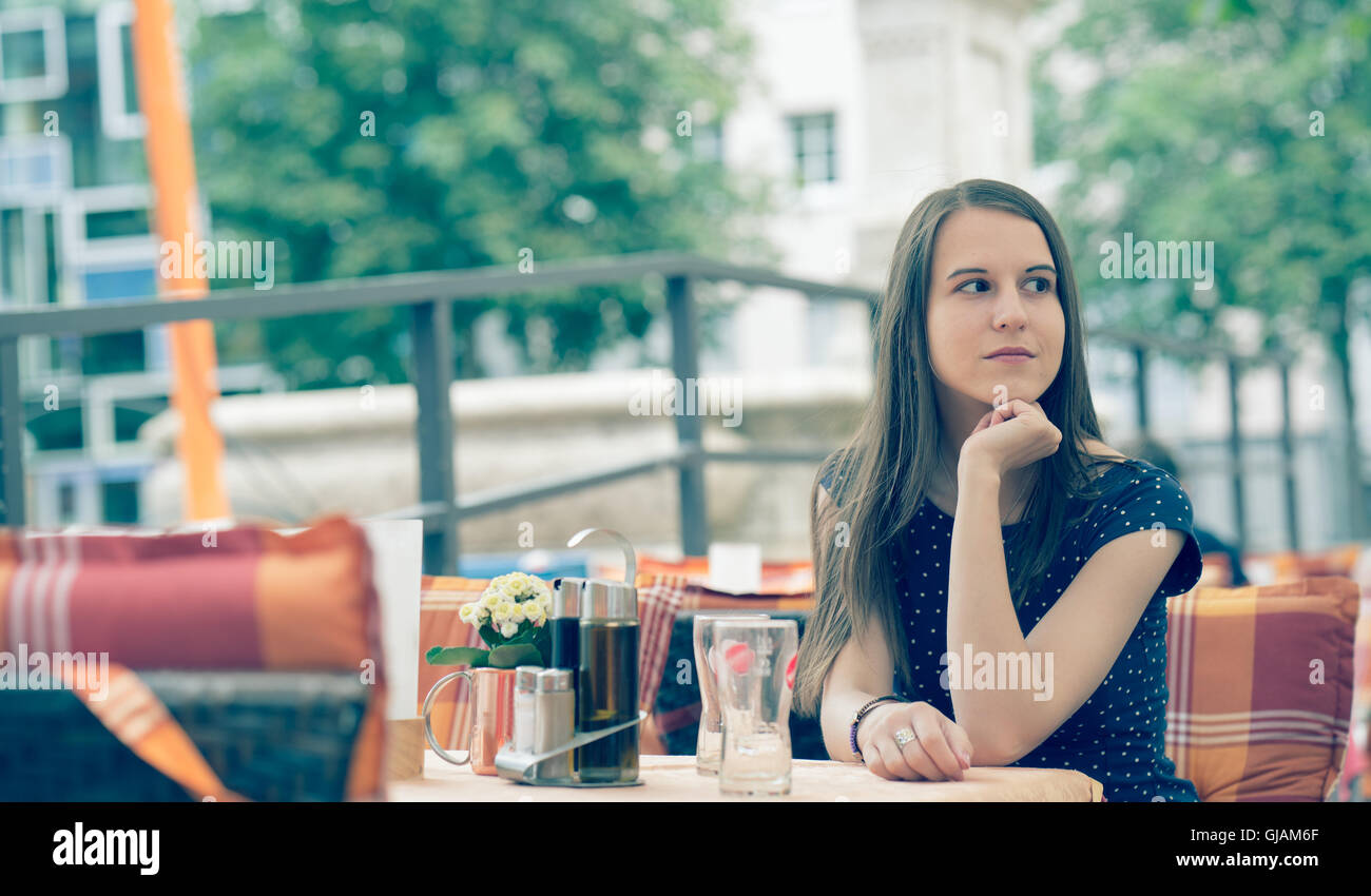 Una ragazza seduta alla caffetteria all'aperto con tavolo e in attesa per il caffè Foto Stock