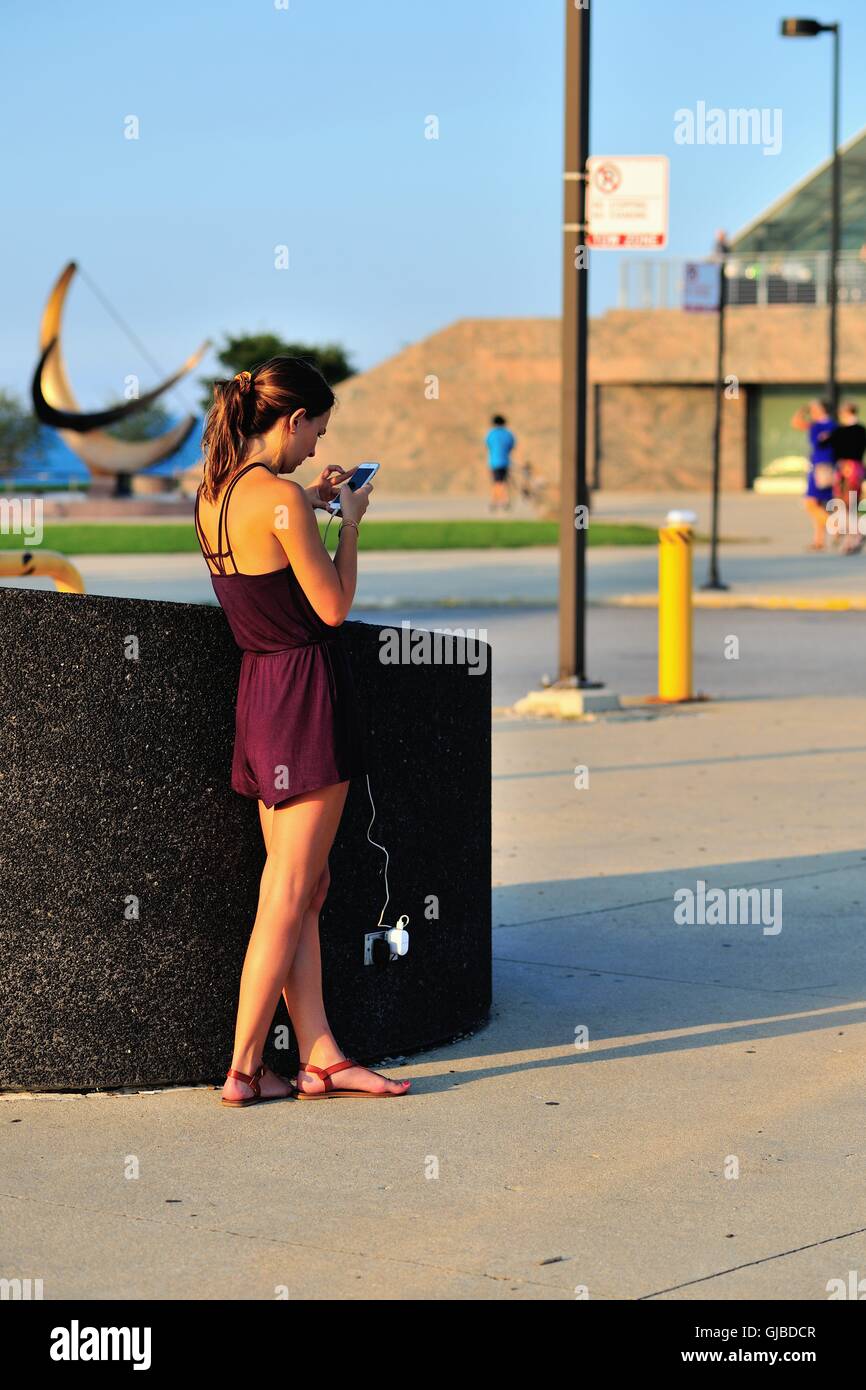 Una giovane donna assume il vantaggio di una piscina presa elettrica per ricaricare il suo cellulare mentre anche utilizzando il dispositivo. Chicago, Illinois, Stati Uniti d'America. Foto Stock