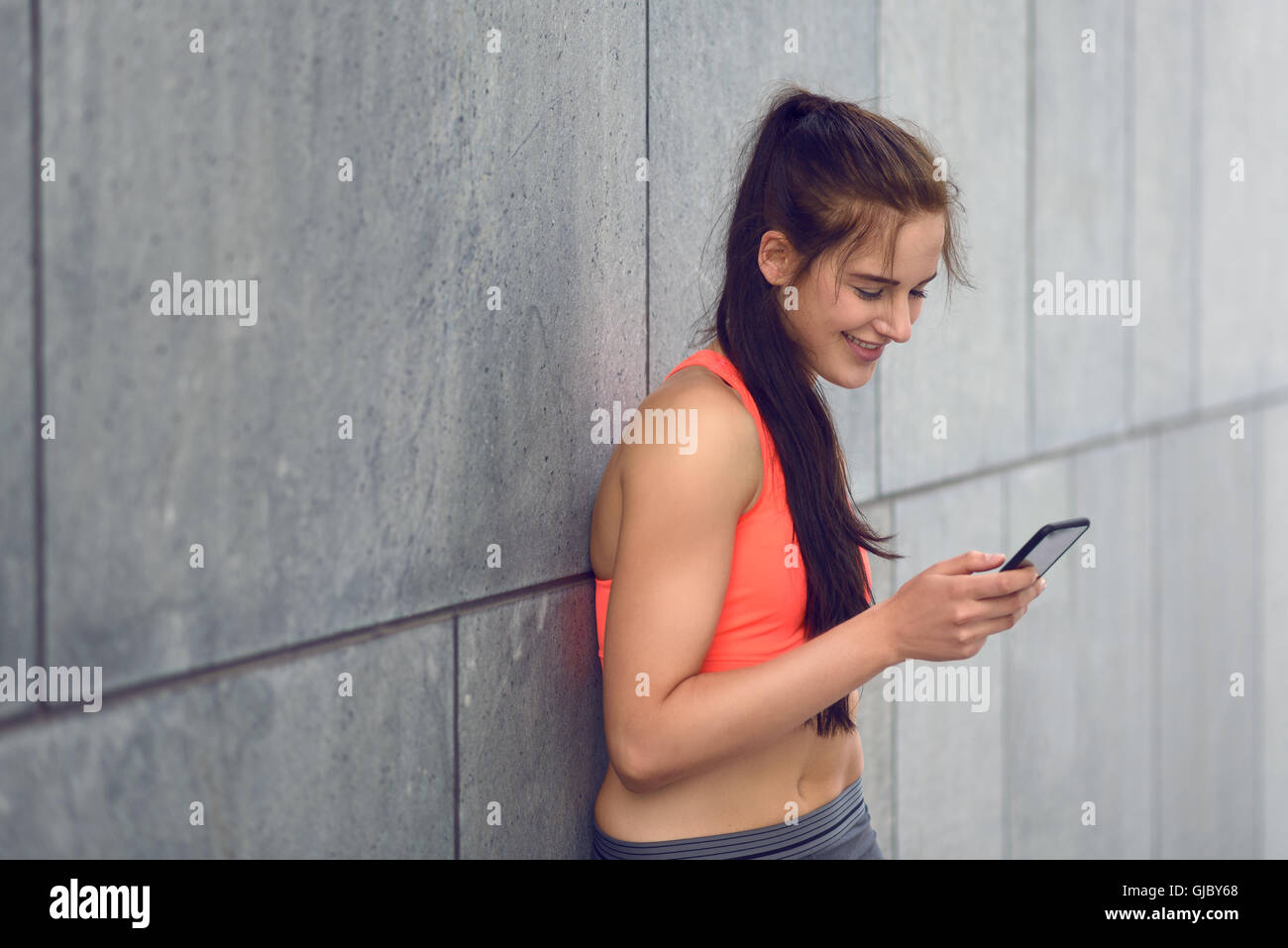 Sporty giovane donna in piedi appoggiata contro il muro di un edificio controllo dei suoi messaggi sul suo telefono , con spazio di copia Foto Stock