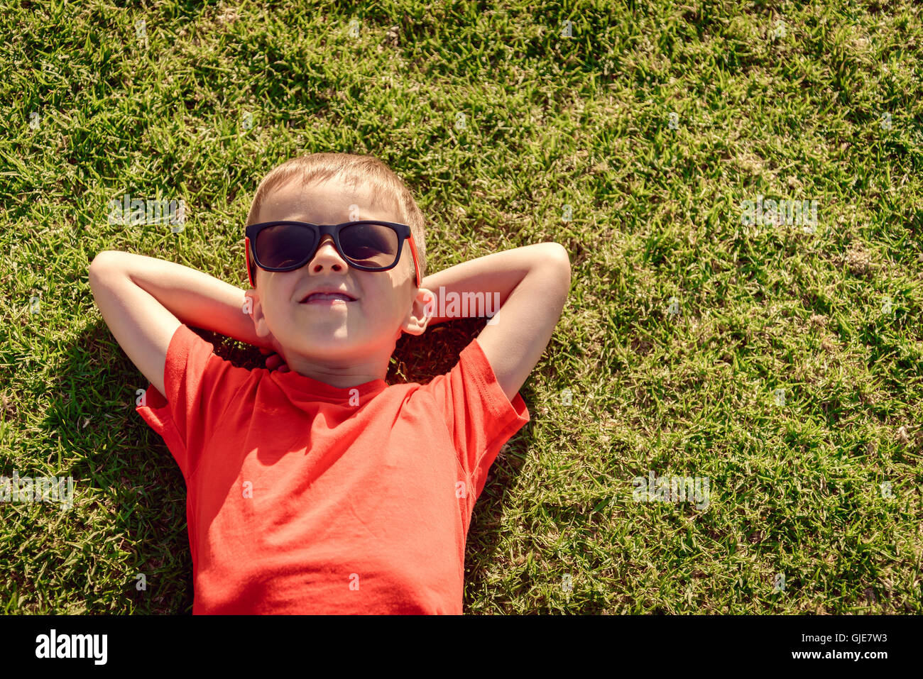 Sorridenti boy rilassante sull'erba, vista dall'alto. Color-tonificante applicato Foto Stock