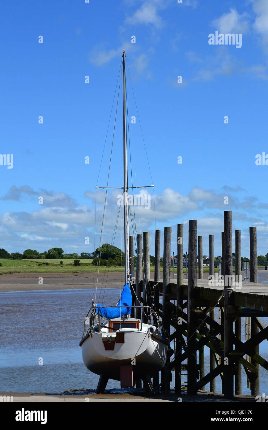 Singolo Yacht a vela arrotolata sulla terraferma da un pontile in legno sul fiume Wyre a Skippool Creek, LANCASHIRE REGNO UNITO Foto Stock