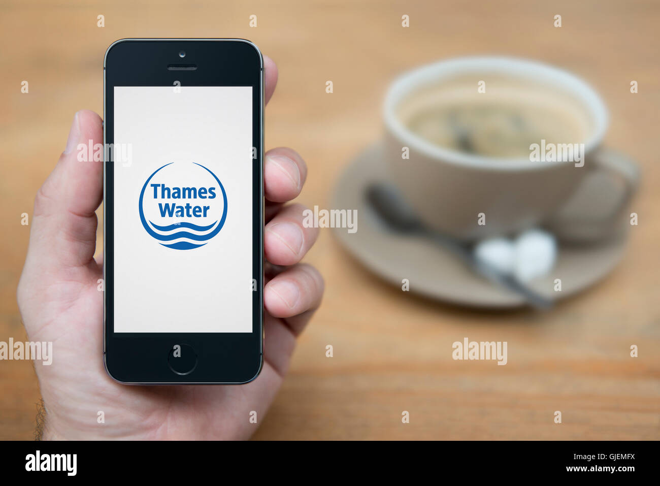 Un uomo guarda al suo iPhone che visualizza la Thames Water logo, mentre sat con una tazza di caffè (solo uso editoriale). Foto Stock