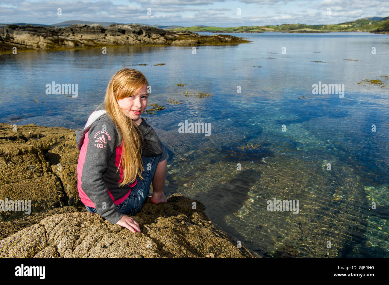 Una bella 9 anno vecchia ragazza seduta sulle rocce di mare in West Cork, Irlanda con copia spazio. Foto Stock