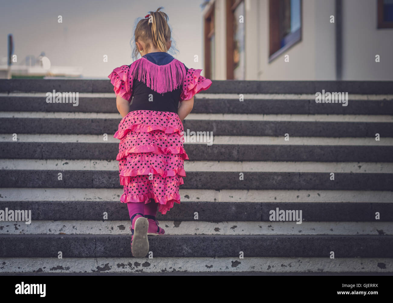 Poco quattro anni ragazza vestita in salsa rosa costume salendo le scale in città Foto Stock
