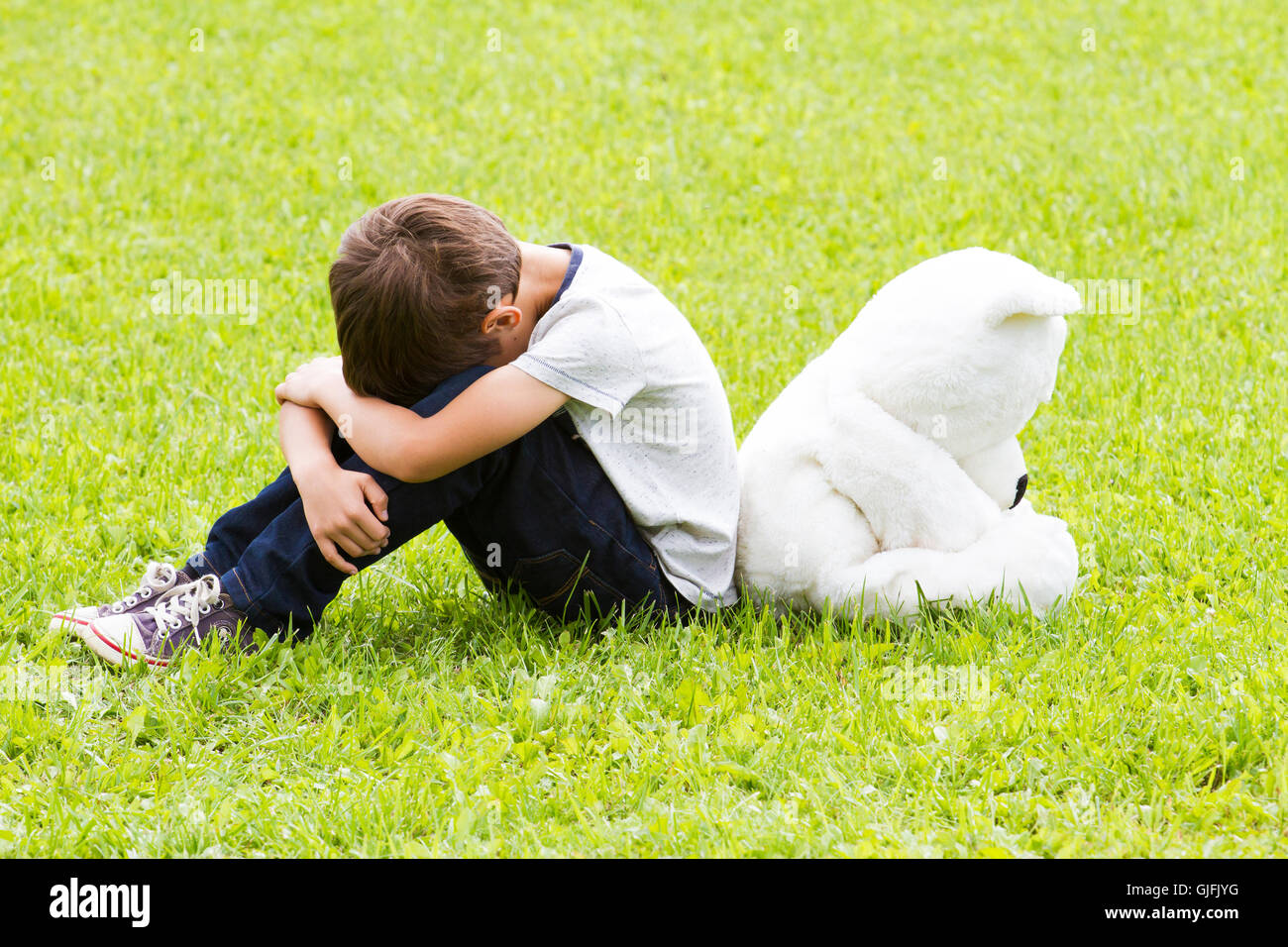 Triste piccolo ragazzo seduto con un orsacchiotto di peluche. Entrambi si voltò e abbassato le loro teste. Tristezza, paura, frustrazione e di solitudine concept Foto Stock