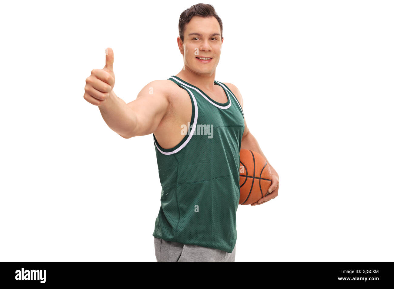 Uomo sorridente in una maglia verde tenendo una palla da basket e dando un pollice in alto isolato su sfondo bianco Foto Stock