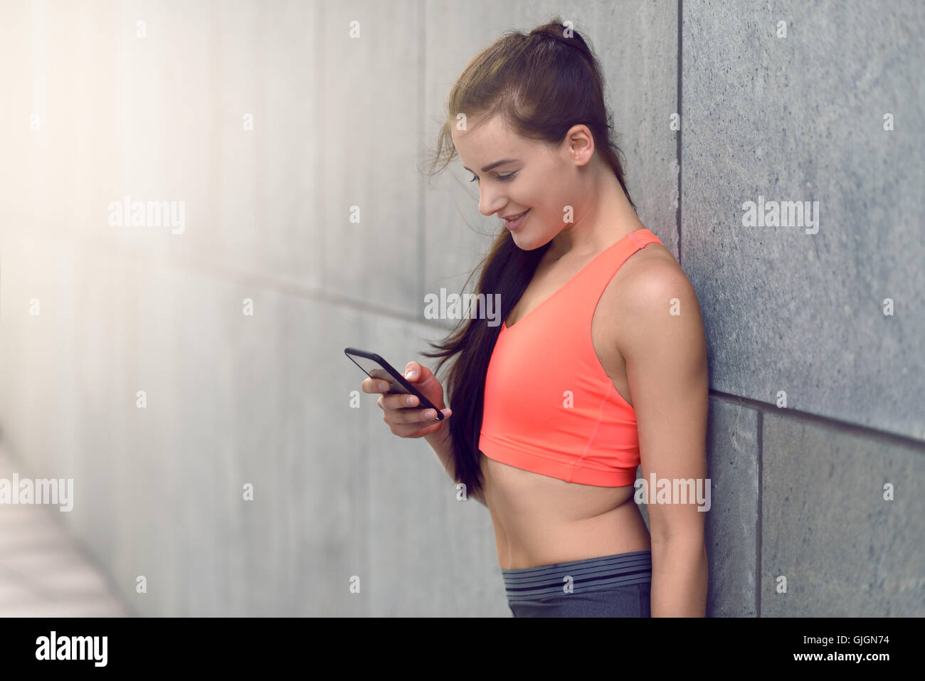 Sporty giovane donna in piedi appoggiata contro il muro di un edificio controllo dei suoi messaggi sul suo telefono , con spazio di copia Foto Stock