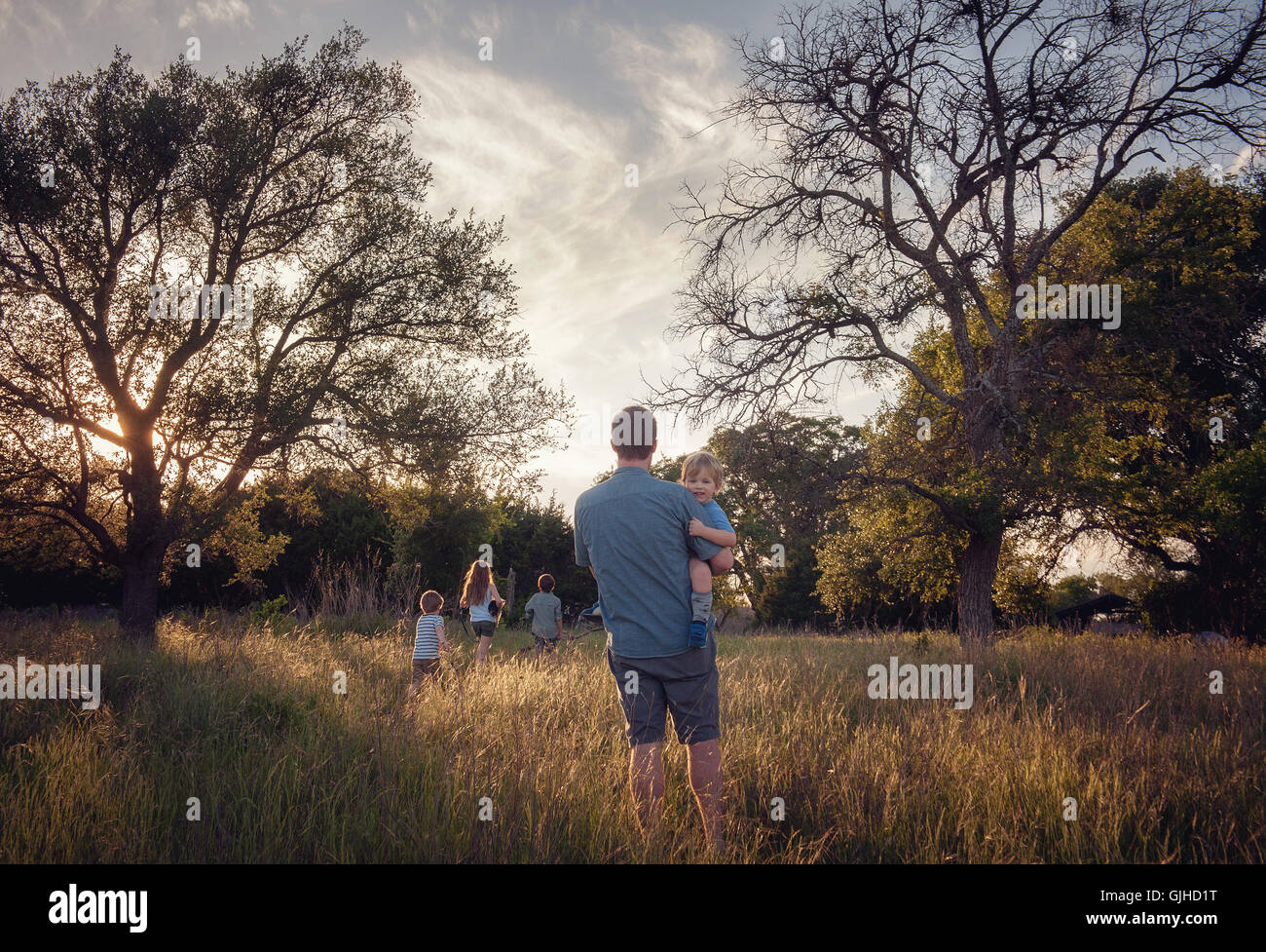 Padre e quattro bambini che camminano nel paesaggio rurale al crepuscolo, Texas, Stati Uniti Foto Stock