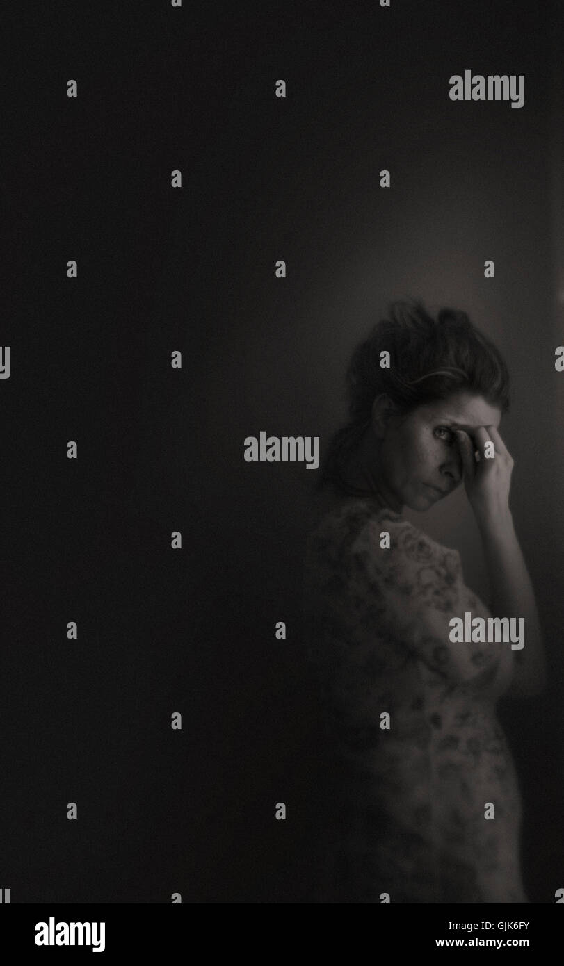 Triste,giovane donna in piedi in camera dalla finestra che copre il volto Foto Stock